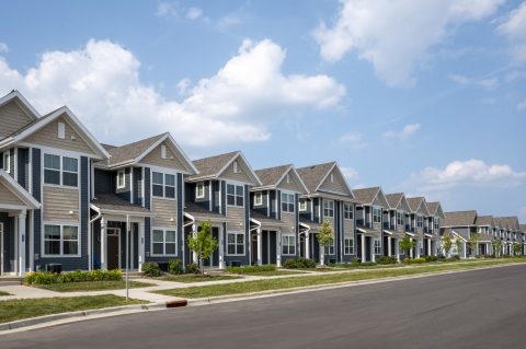Row of modern townhouses with well-maintained lawns and clear blue sky.