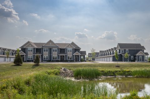 Contemporary apartment buildings with landscaped surroundings and a pond in the foreground.
