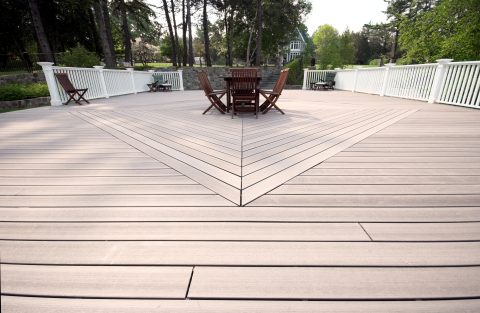 Spacious outdoor deck with wooden flooring and white railing, surrounded by trees.