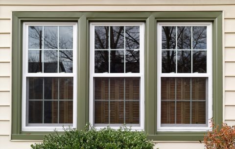Triple window with white frames and green trim on a house exterior.