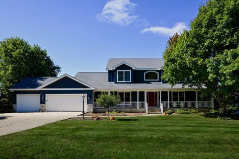 Modern house with a large front porch, two-car garage, and lush green lawn.