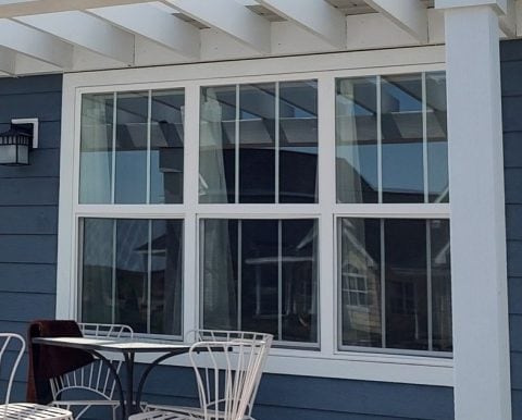 Large white-framed windows on a blue house exterior with patio furniture.