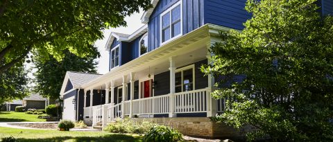 Beautiful blue house with white porch and lush green trees.
