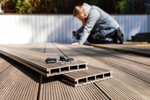 Man installing composite decking boards on outdoor patio.