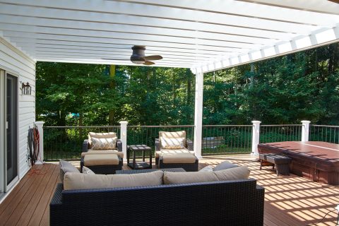 Spacious outdoor deck with seating, hot tub, and lush green trees in background.