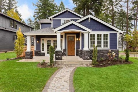 Modern blue house with white trim and stone accents, surrounded by lush green lawn and trees.