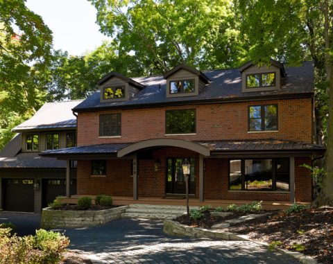 Beautiful brick house with large windows and lush greenery in the background.