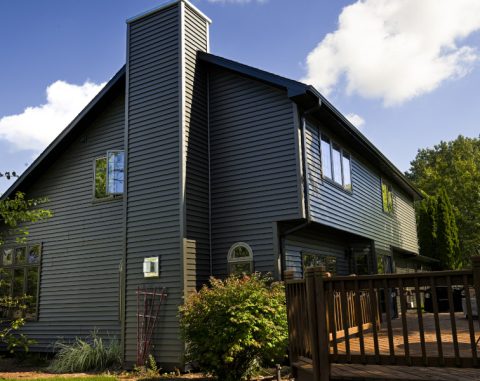 Contemporary house with dark siding and large windows under a blue sky.