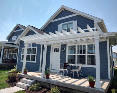 Beautiful blue house with white pergola and outdoor seating area.
