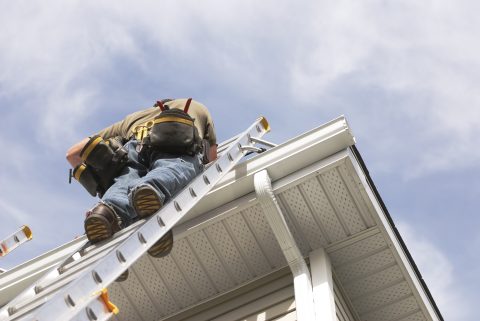 Roofing contractor inspecting roof from ladder for home exterior project.