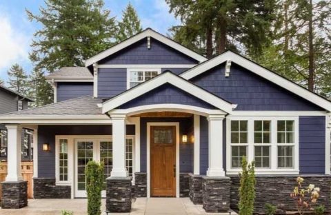 Beautiful modern house with blue siding, white trim, and large windows in a wooded area.