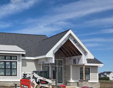 House with new siding and roof under construction, blue sky background.