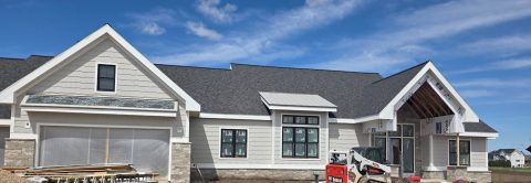 Newly constructed house with white siding, large windows, and a gabled roof under a blue sky.