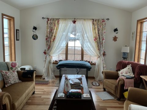 Bright living room with large windows, floral curtains, and comfortable furniture.