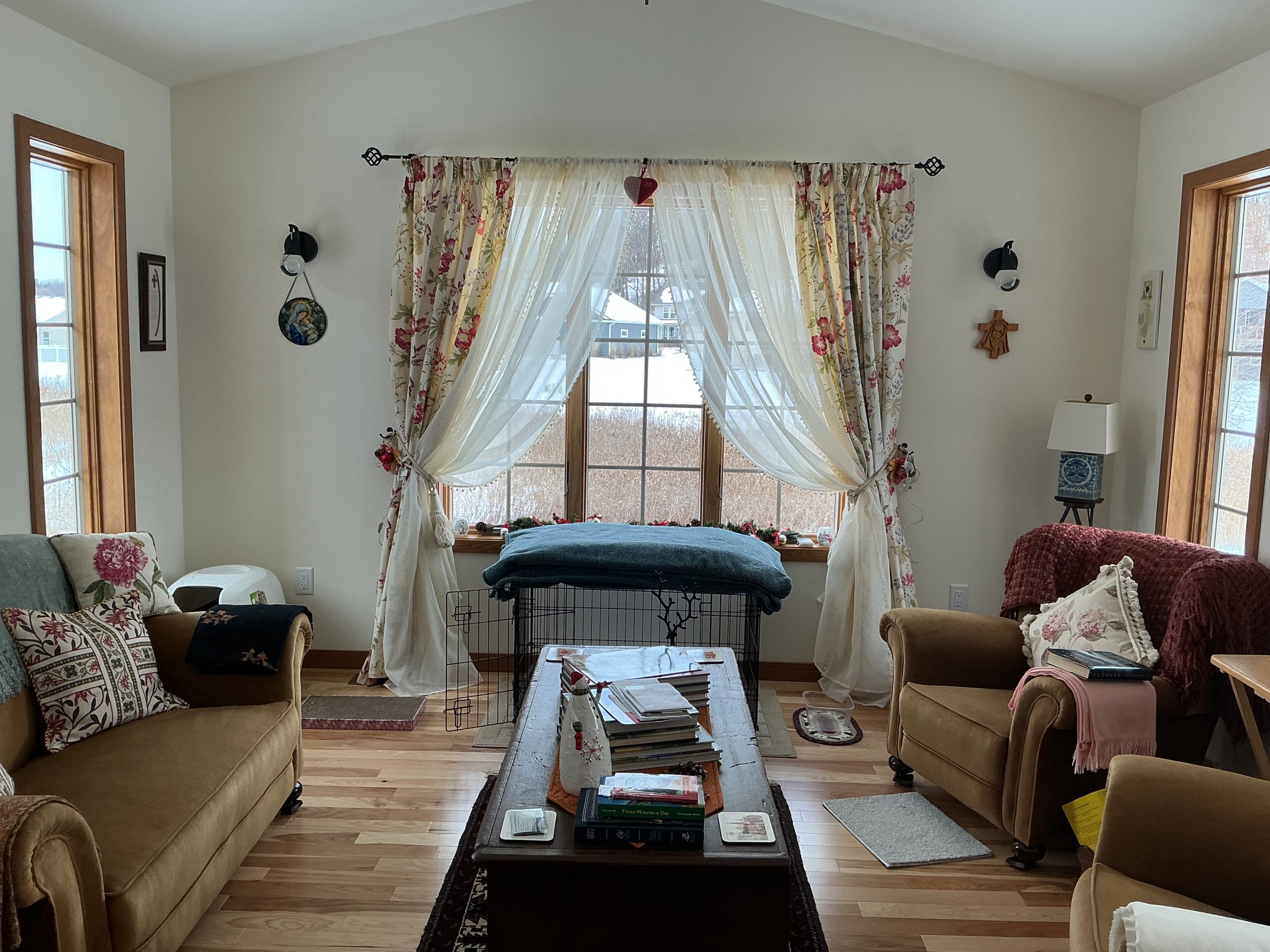 Bright living room with large windows, floral curtains, and comfortable furniture.