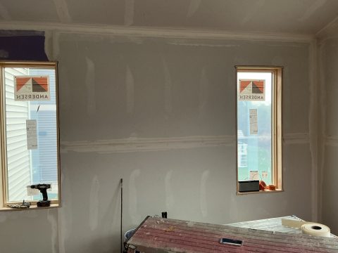 Interior drywall installation with two windows in progress.