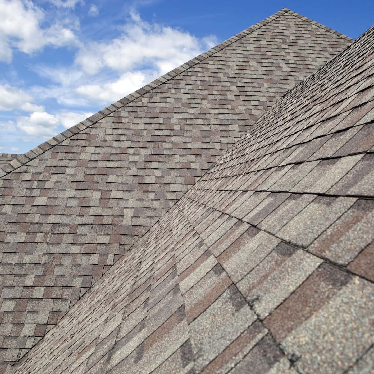 Close-up of asphalt shingle roofs with blue sky background.