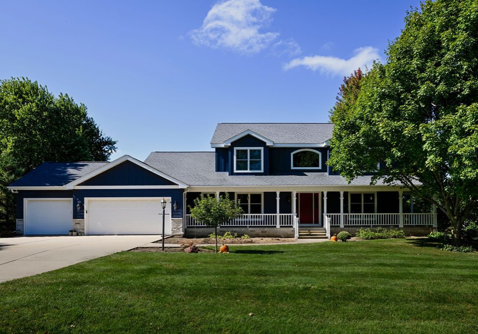 Modern house with a large front porch, two-car garage, and lush green lawn.