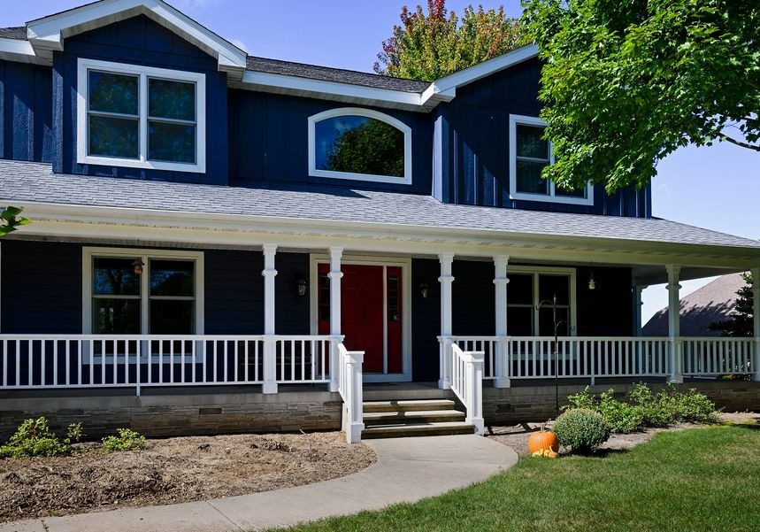 Modern blue house with white porch railing and lush green yard.