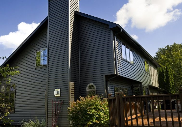 Contemporary house with dark siding and large windows under a blue sky.