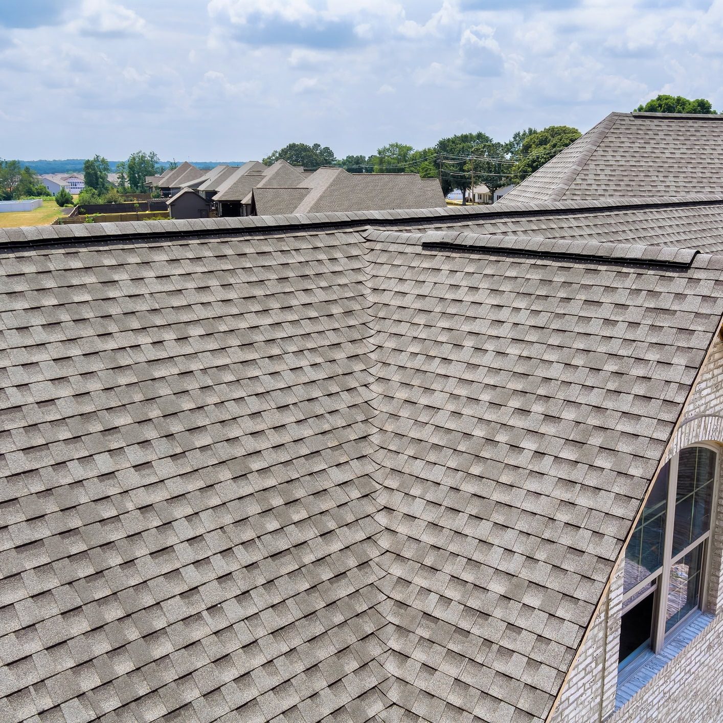 Close-up of a residential roof with new asphalt shingles in a suburban neighborhood.